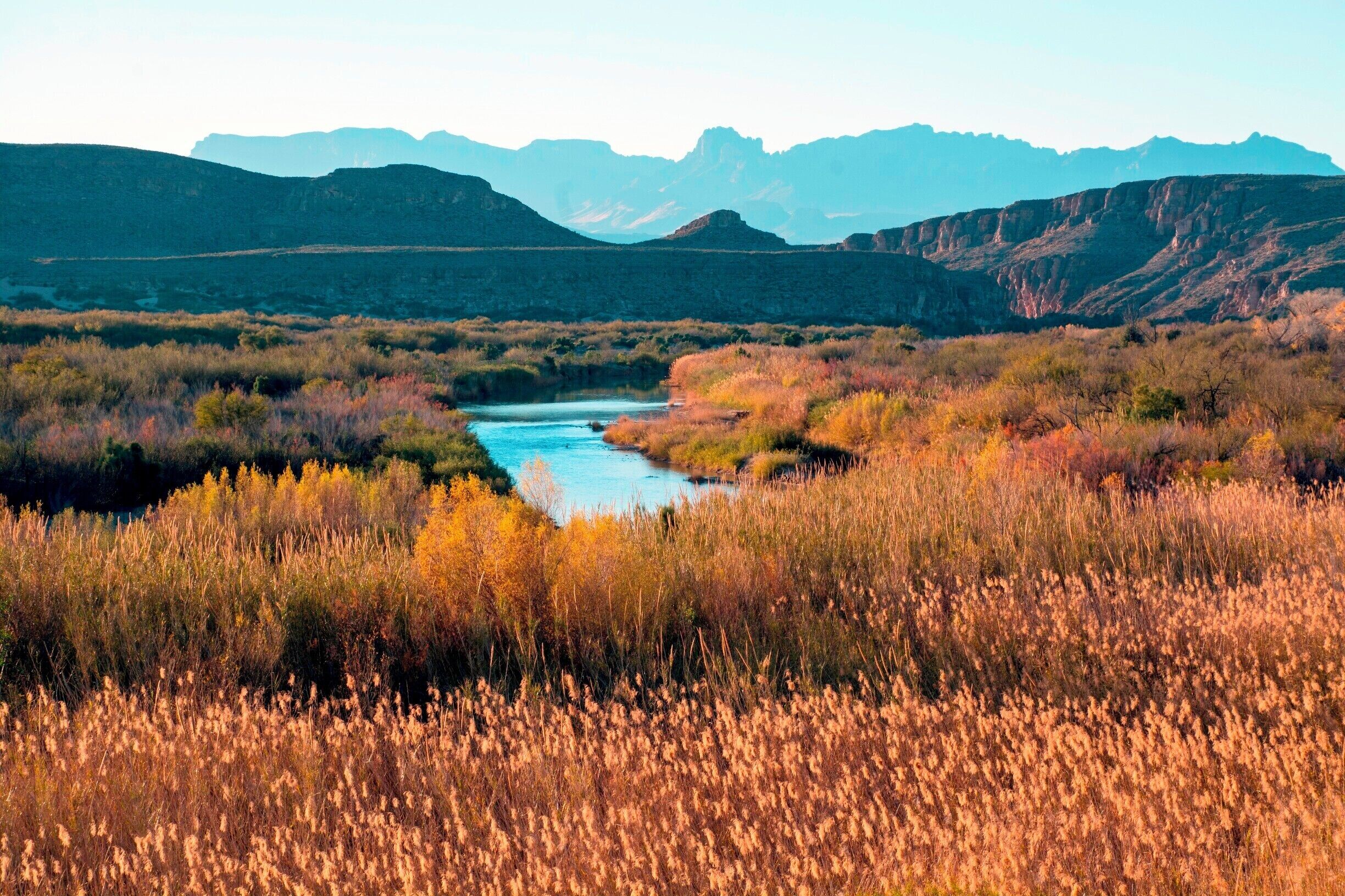 A river winding through a valley with autumn-colored vegetation and distant mountains.