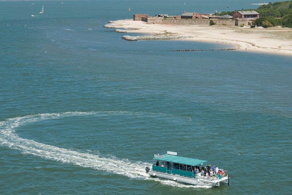 A boat on a calm sea with a sandy beach and buildings in the background.