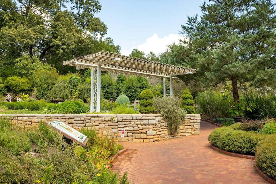 A garden with a pergola, stone wall, and a pathway.