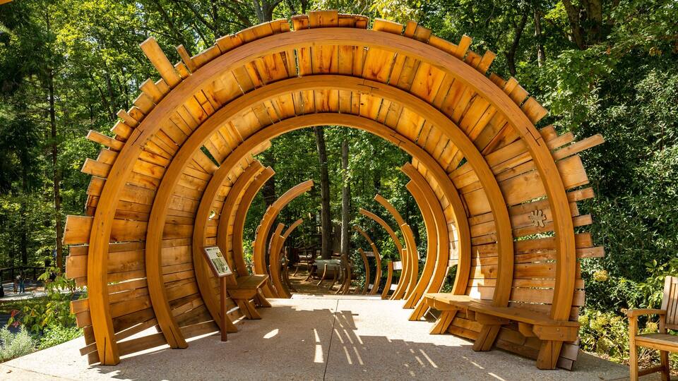 A wooden archway with benches, surrounded by trees.