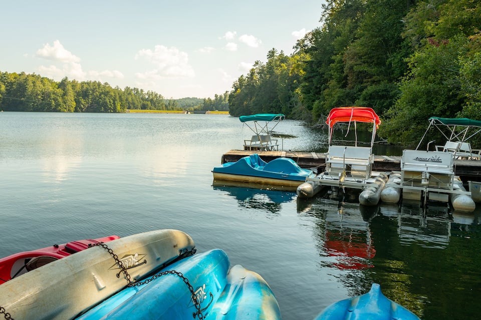 A calm lake with boats docked at a pier, surrounded by dense forest.