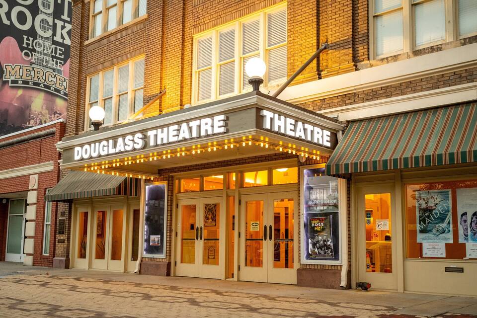 Exterior del Teatre Douglass amb llums de la cartelera i pòsters anunciant espectacles.