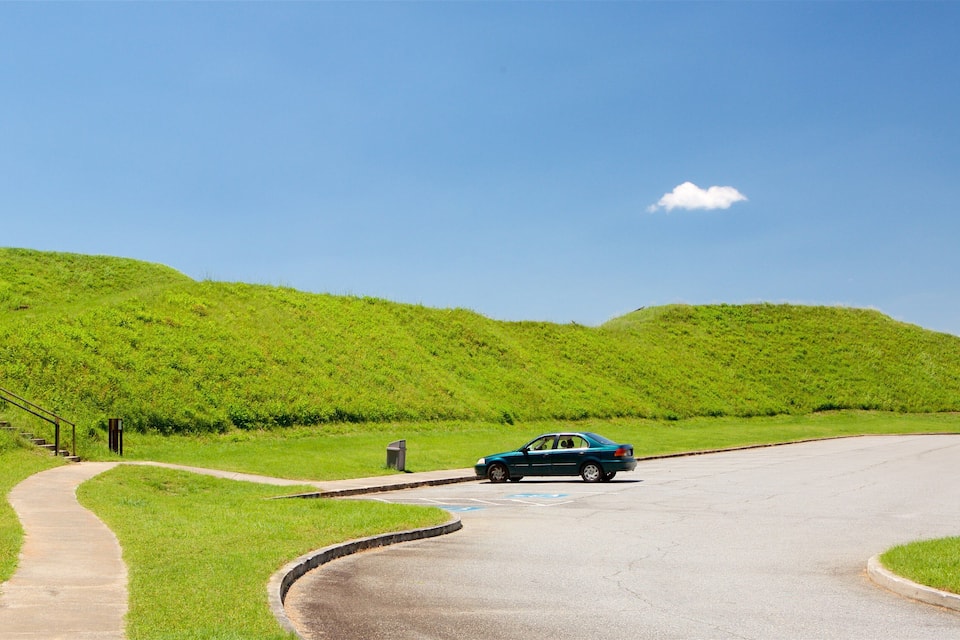 A car on a winding road with grassy hills in the background.