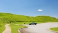A car on a winding road with grassy hills in the background.