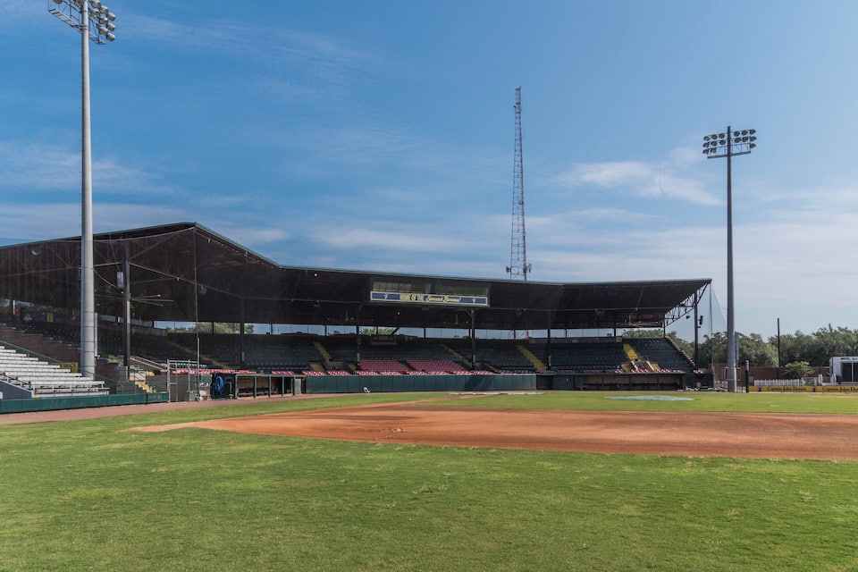 A baseball stadium with empty stands, a clear sky, and a large scoreboard.