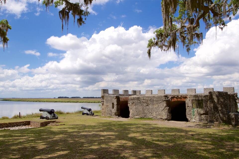 A historic fort with cannons by a lake, surrounded by trees and a clear sky.