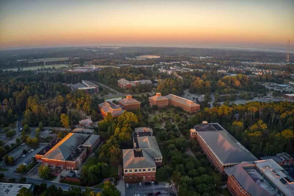 Vista aérea de un campus universitario con varios edificios, rodeado de árboles y campos abiertos.