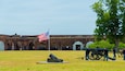 A historic fort with a flagpole, cannons, and a large tree.