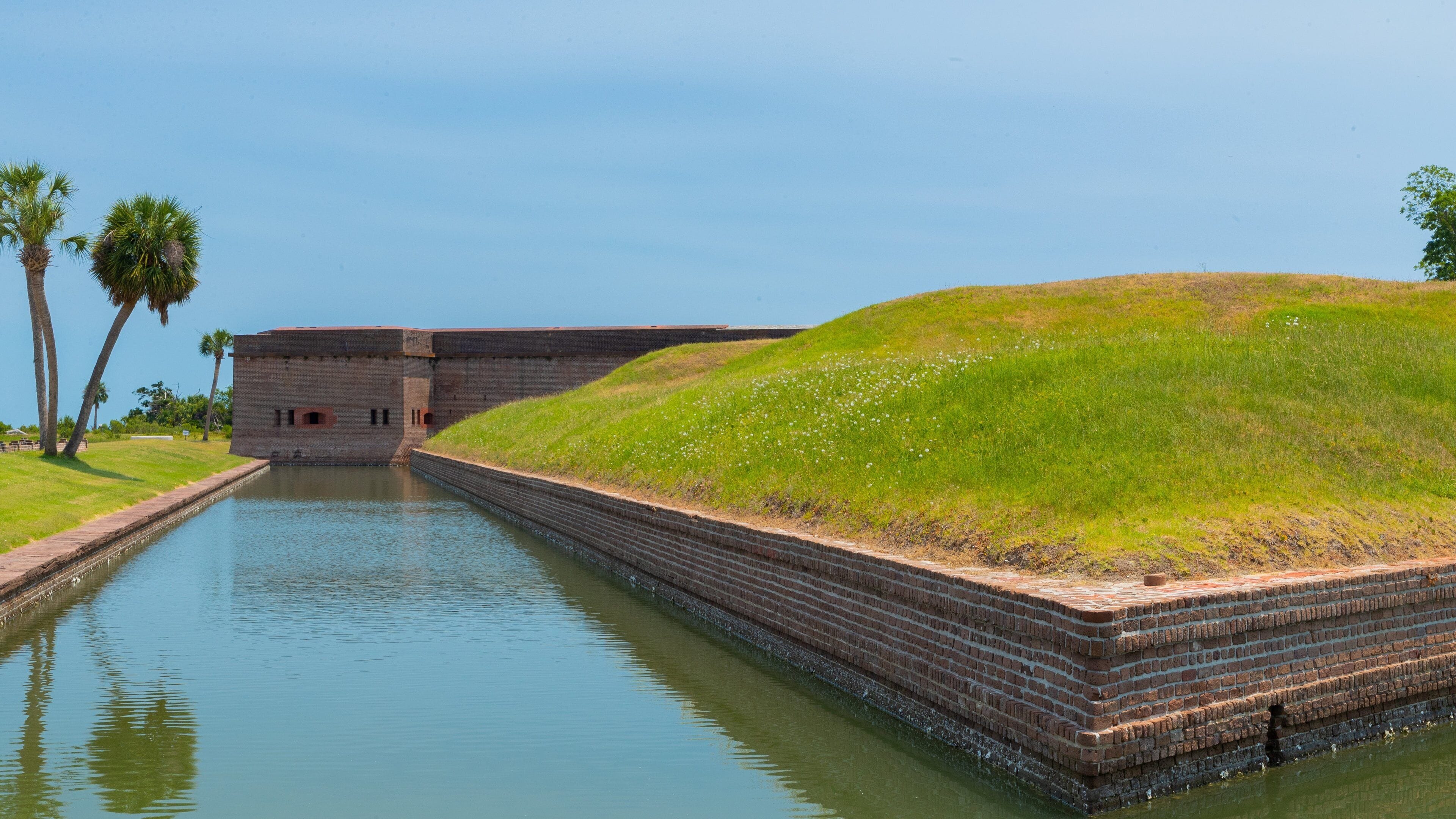 A brick fort with a grassy hill and palm trees.