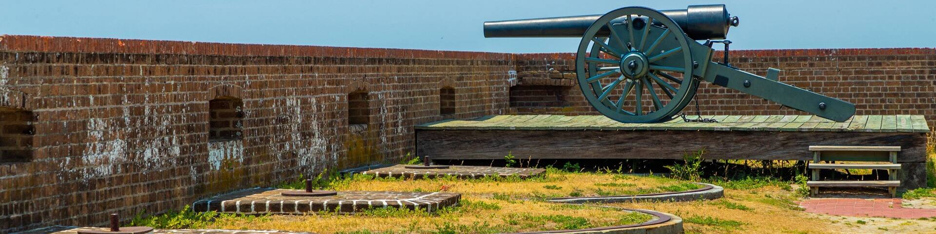A large cannon in a grassy field with a brick wall in the background.