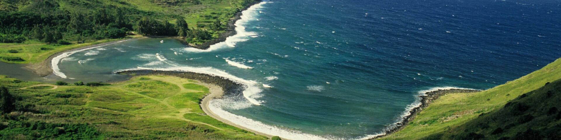A coastal landscape with a green hill, a curved shoreline, and the ocean.