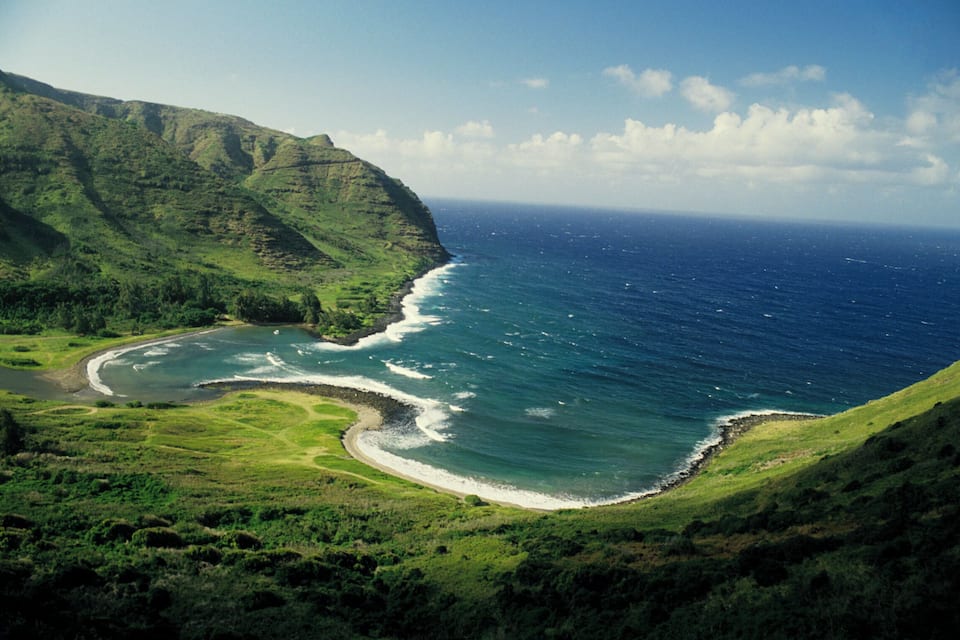 A coastal landscape with a green hill, a curved shoreline, and the ocean.