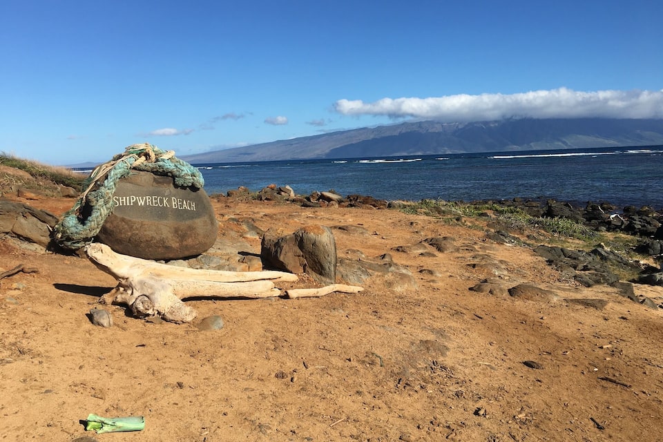 A rocky beach with a large stone labeled "Shipwreck Beach" and a wooden log.