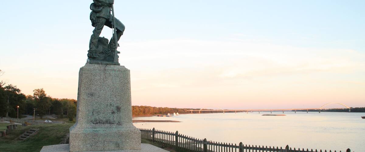 A statue of a soldier on a pedestal by a river.