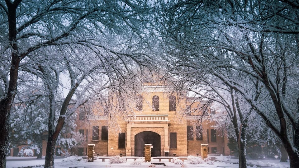 A snow-covered building with a brick facade and arched entrance, surrounded by snow-laden trees.