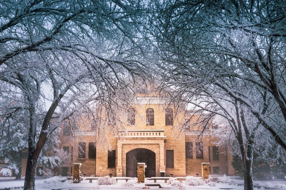 A snow-covered building with a brick facade and arched entrance, surrounded by snow-laden trees.