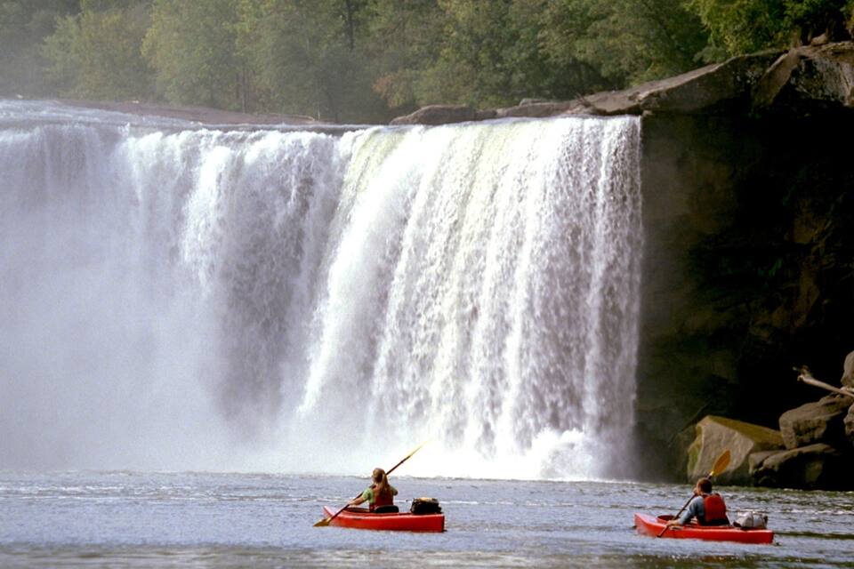 A waterfall with two kayakers in red kayaks.