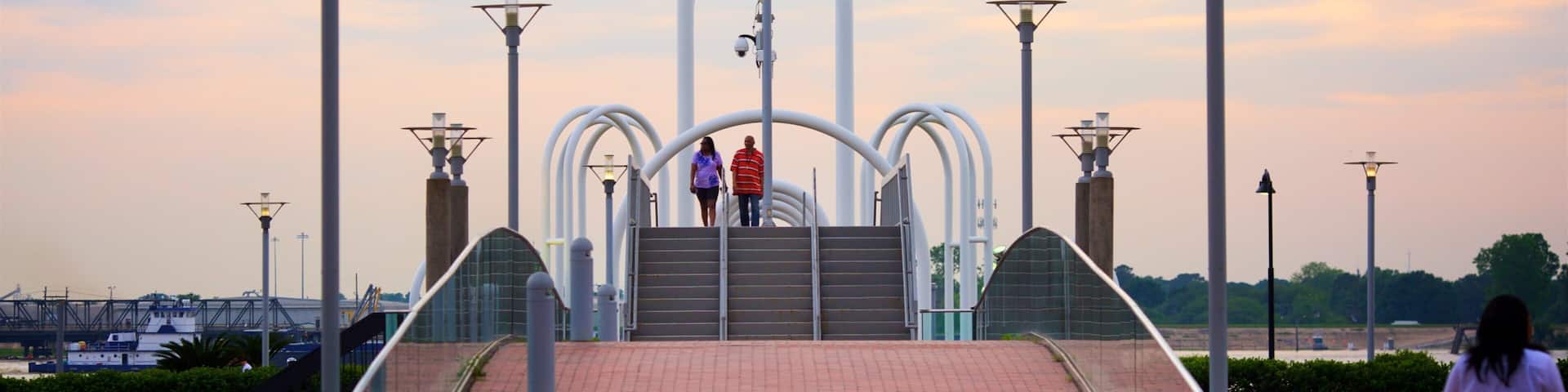 A bridge with a unique arch design, surrounded by street lamps and a sunset sky.