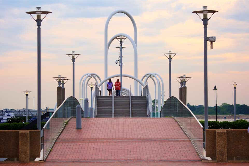 A bridge with a unique arch design, surrounded by street lamps and a sunset sky.