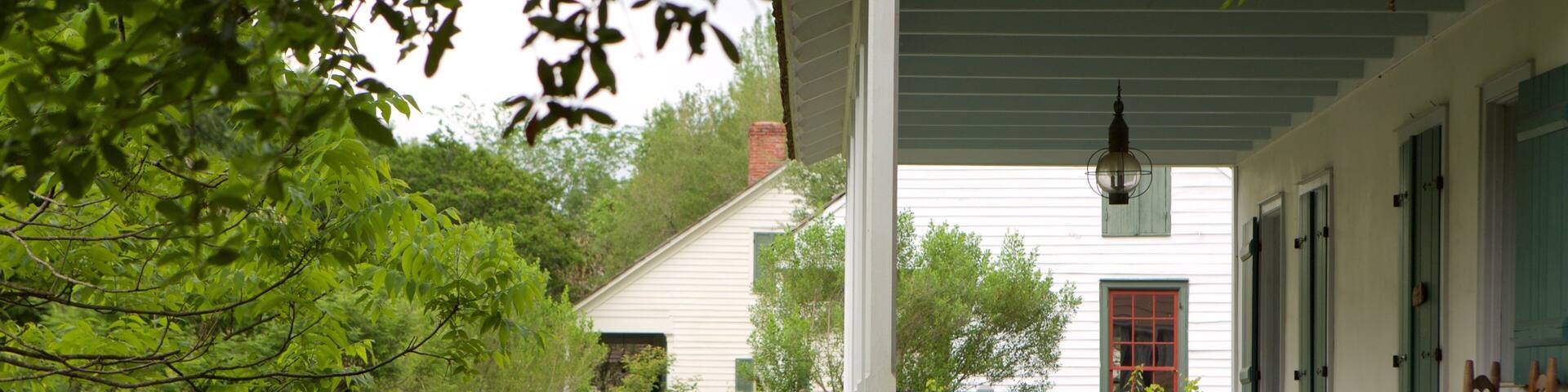 A white house with a green porch, red door, and a wooden fence.