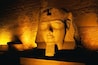 A large stone head sculpture with a flat top, set against a textured wall background.