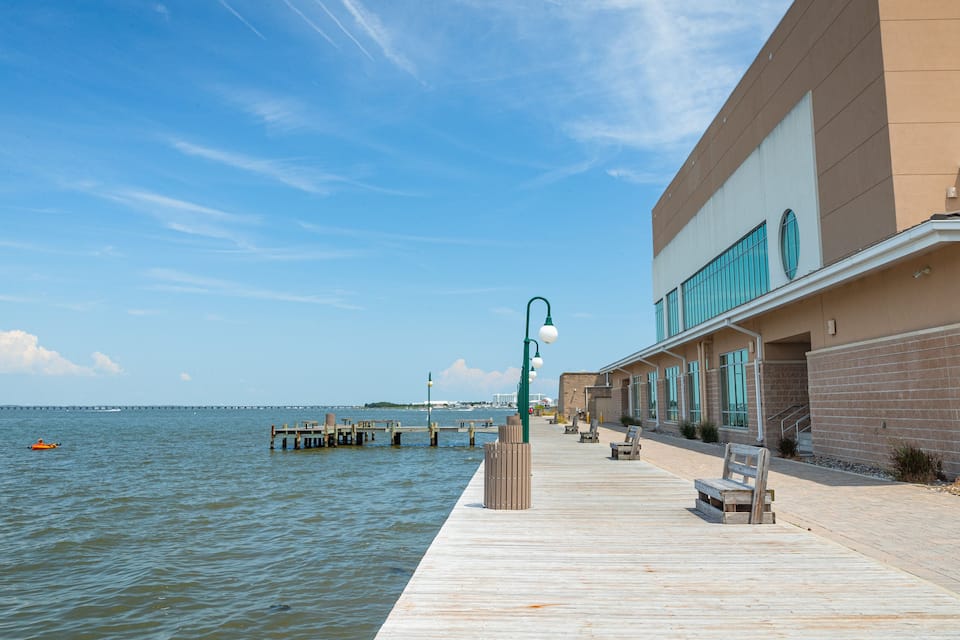 A wooden pier extending into calm waters, a modern building with large windows, and a clear blue sky.