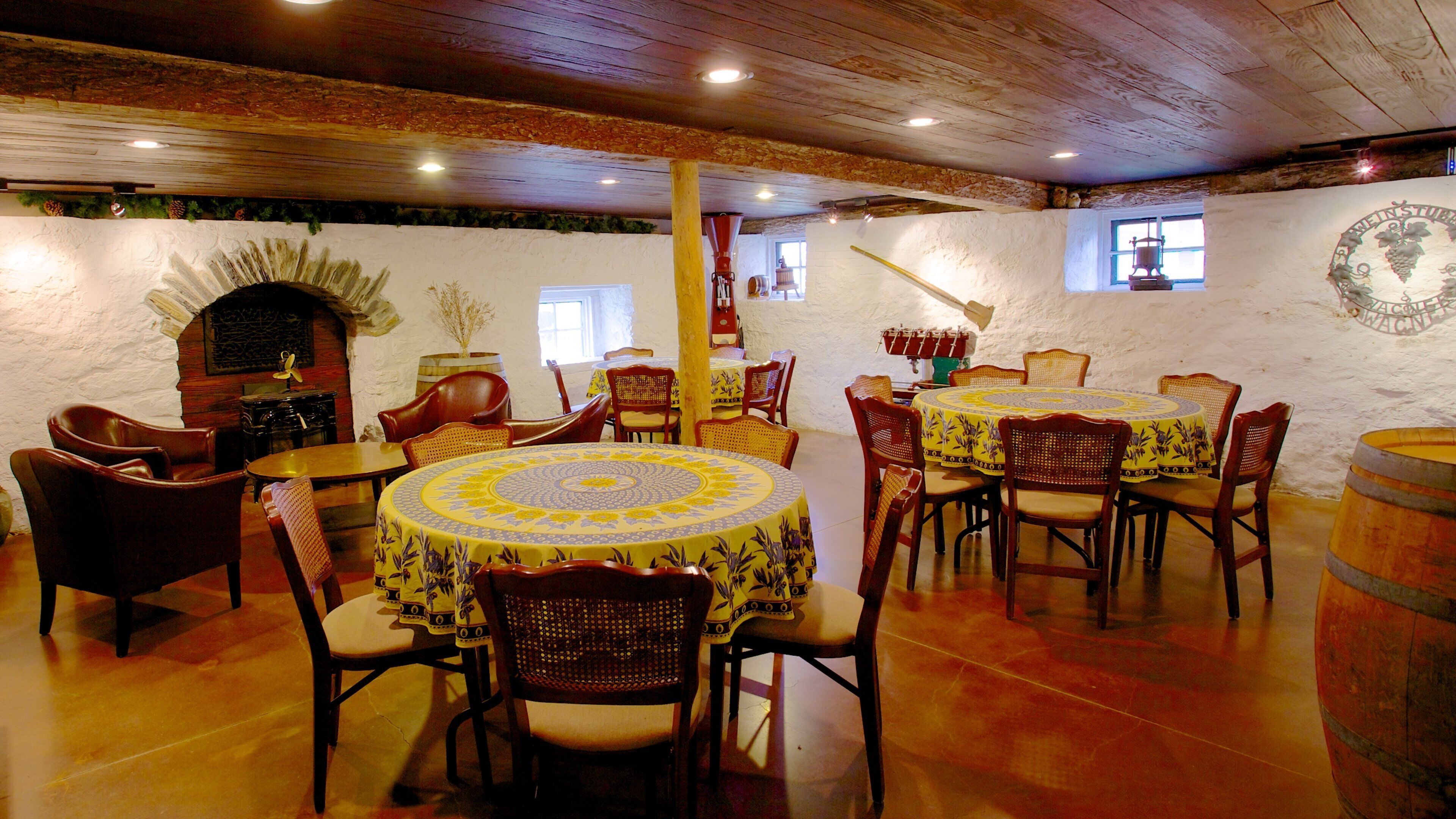 A rustic dining area with wooden tables and chairs, a stone wall, and a barrel.