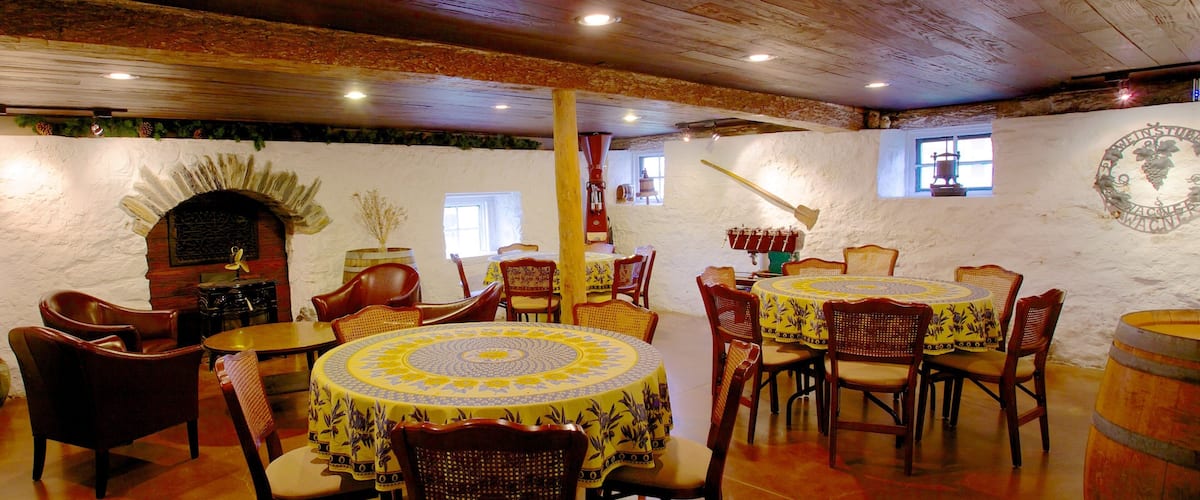 A rustic dining area with wooden tables and chairs, a stone wall, and a barrel.