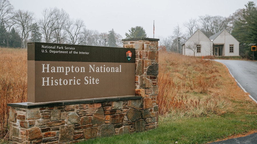 Señal de piedra para el sitio histórico nacional Hampton, con un paisaje rural de fondo.