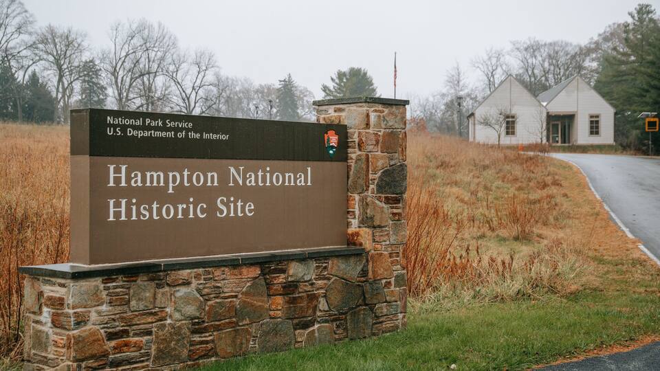 A stone sign for Hampton National Historic Site with a rural landscape in the background.