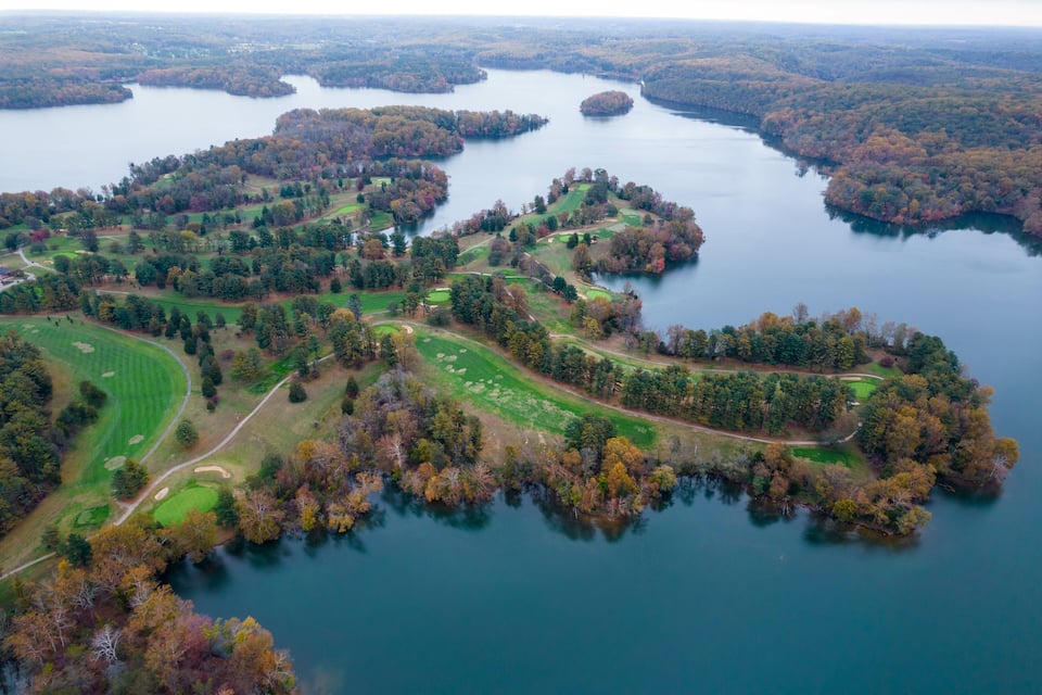 An aerial view of a golf course surrounded by a lake and forested areas.