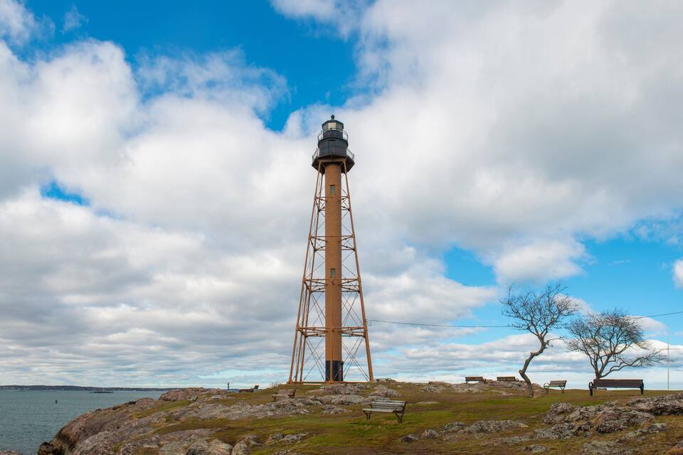 Et fyrtårn på en klippefyldt kyststrækning under en klar himmel med skyer.