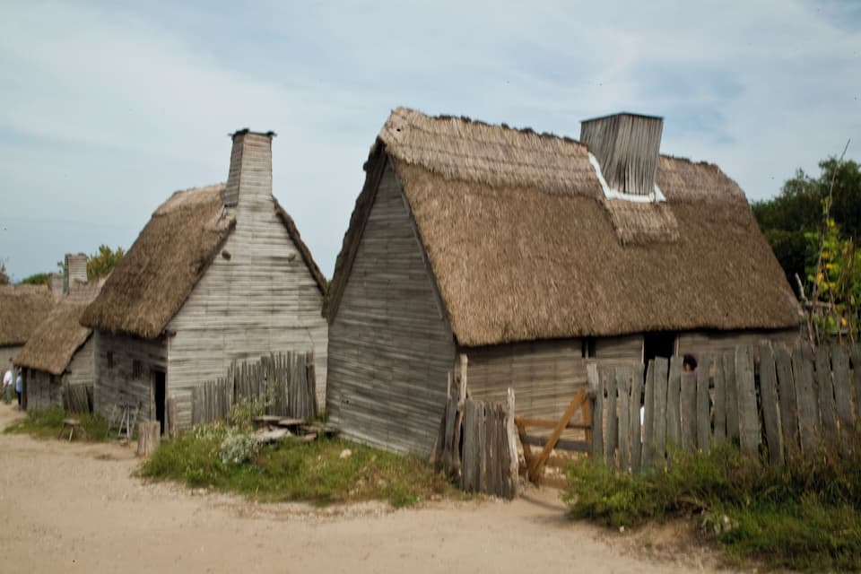 Thatched-roof houses with wooden walls and a dirt path in front.