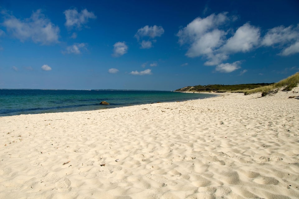 A sandy beach with clear blue water and a few clouds in the sky.