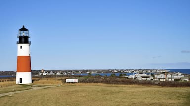 A lighthouse with a white and orange color scheme, a sign indicating it is a Coast Guard station, and a coastal town in the background.
