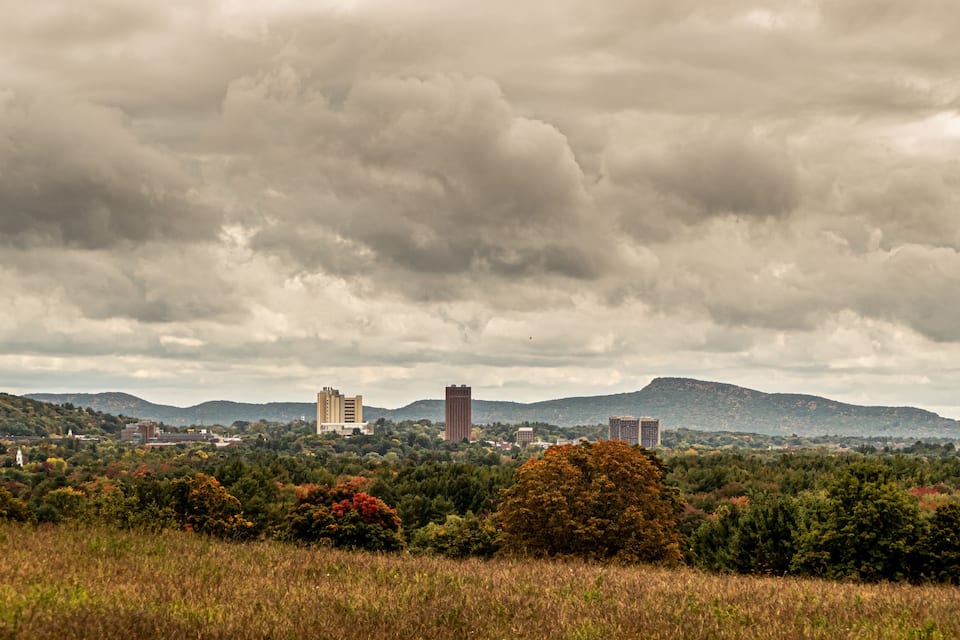 A landscape with a hill, buildings, and a cloudy sky.