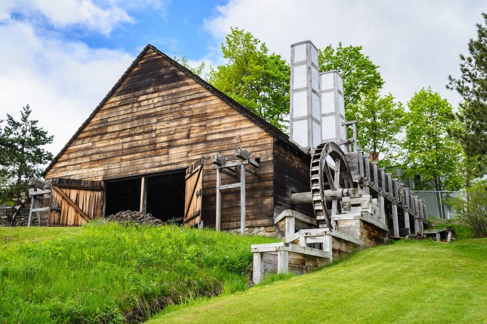 A rustic wooden barn with a large silo and a water wheel.