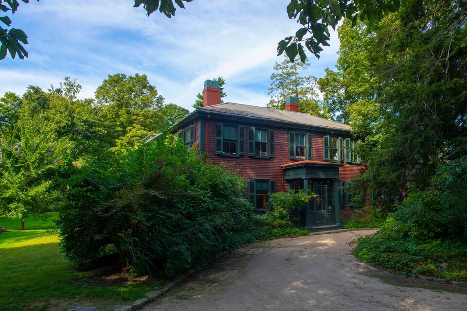 A red brick house with green shutters, surrounded by lush greenery and trees.