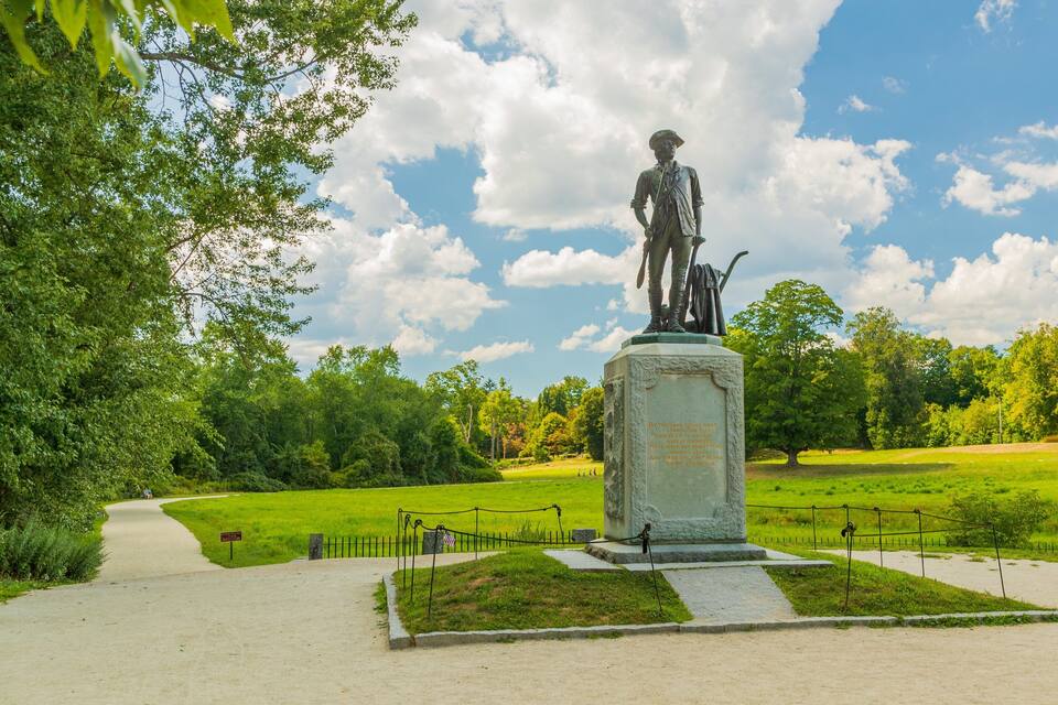 Una estatua en un parque con cielo despejado y árboles verdes.
