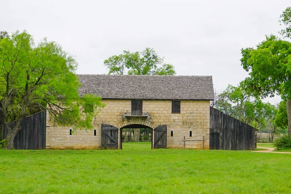 A stone building with a gabled roof, surrounded by green grass and trees.
