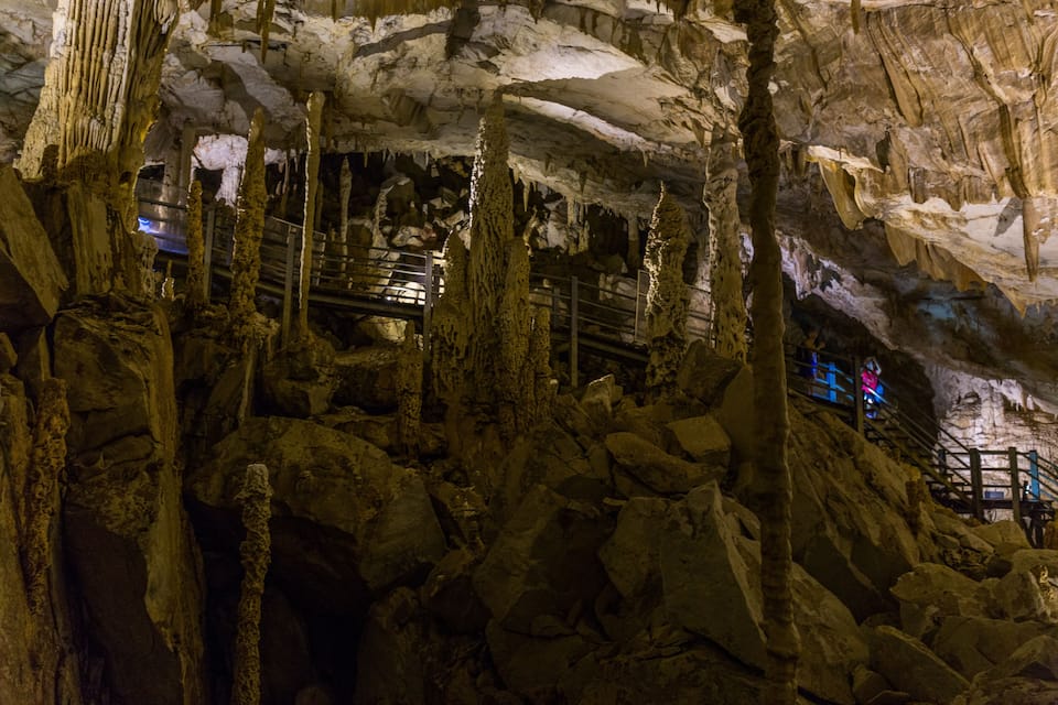 A cave with stalactites and stalagmites, a metal staircase, and a blue-lit area.