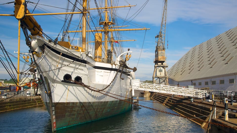 A large sailing ship docked at a port with a crane and a building in the background.