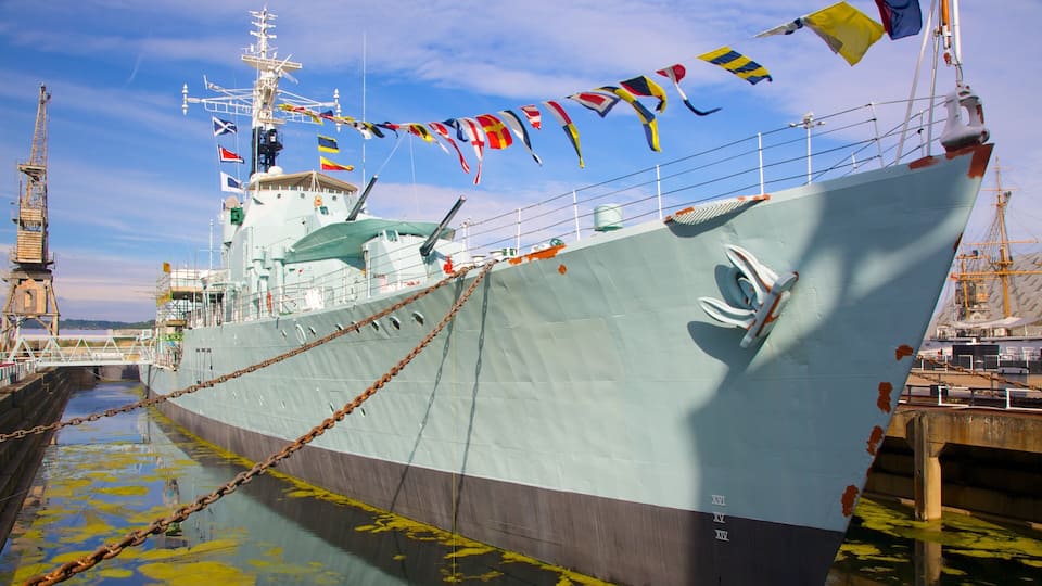 A large ship docked at a port with colorful flags, a bridge, and a clear sky.