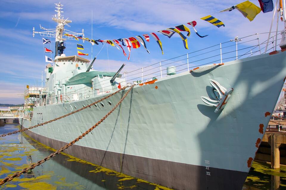 A large ship docked at a port with colorful flags, a bridge, and a clear sky.