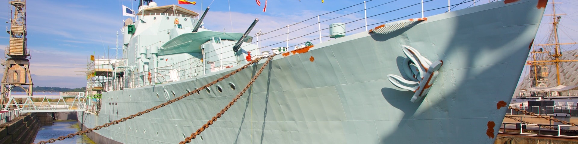 A large ship docked at a port with colorful flags, a bridge, and a clear sky.