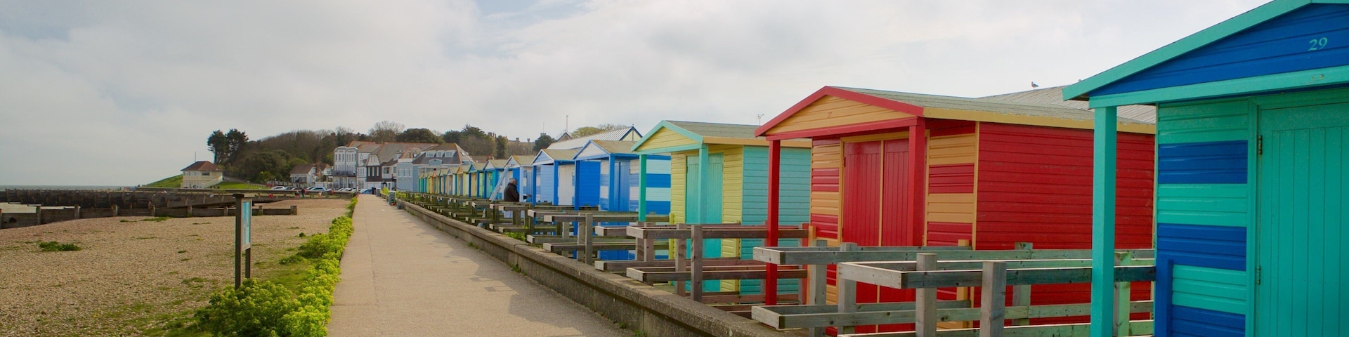 Un paseo marítimo con cabañas de playa coloridas y una playa de guijarros.