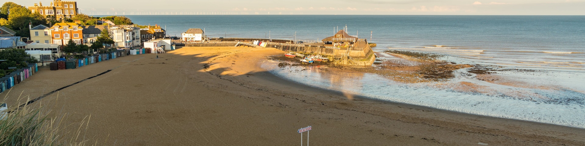 A coastal beach with a rocky outcrop, a pier, and colorful buildings in the background.