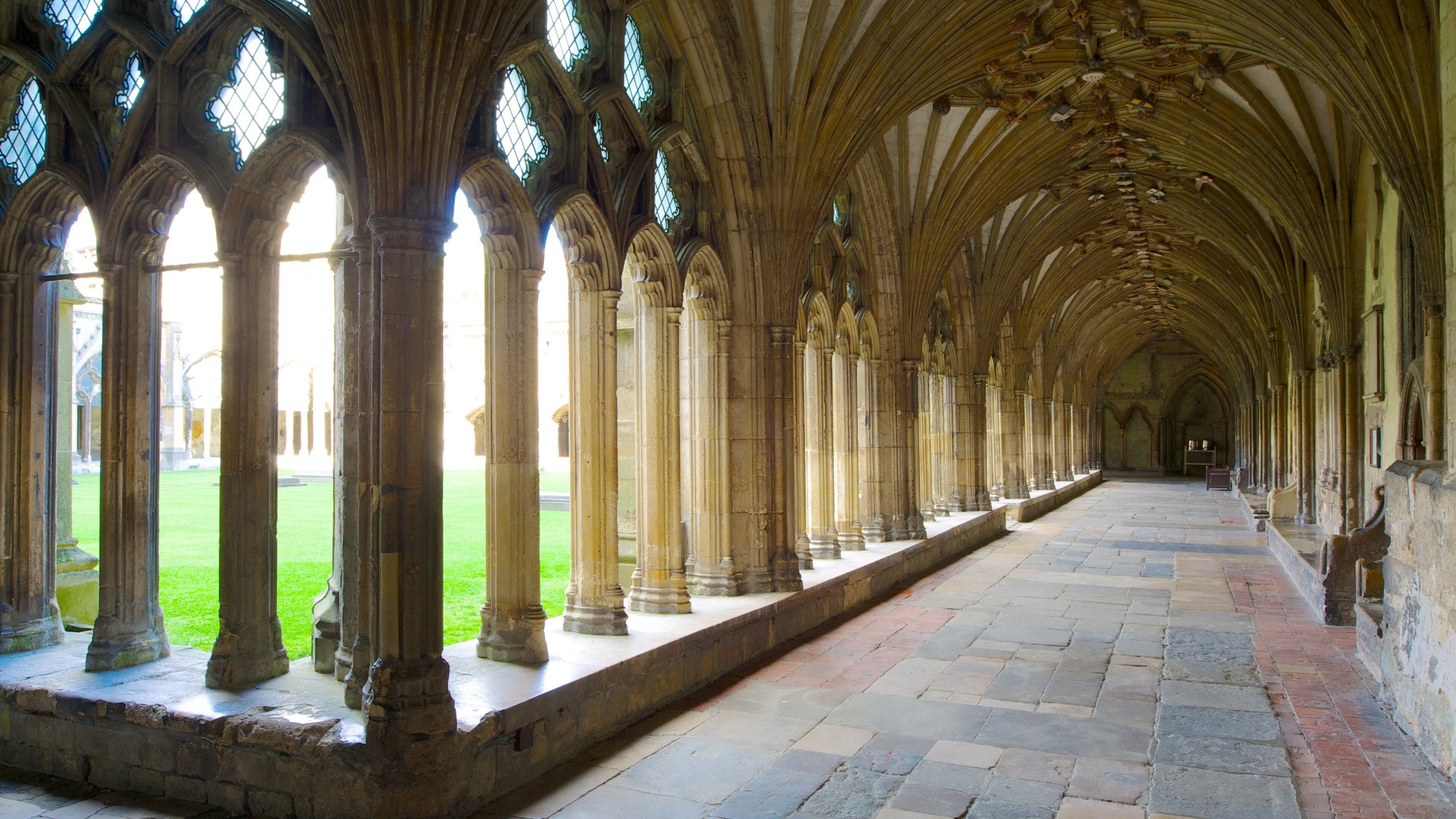 A long corridor with arched ceilings and columns, leading to a courtyard with a lawn.