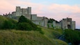 A historic castle on a grassy hill with a paved path leading to it.
