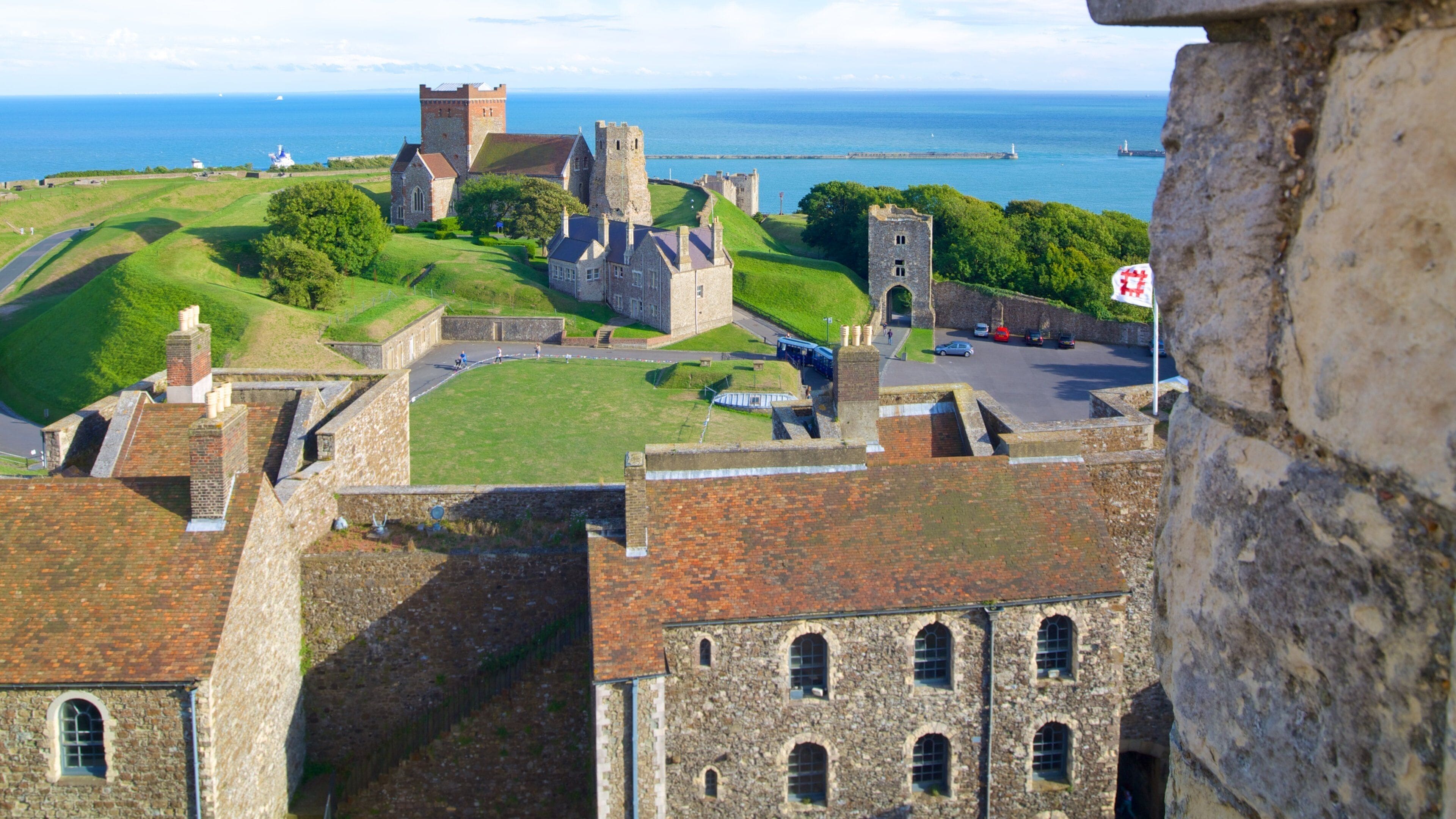 A historic castle complex with a large tower, a church, and a coastal view.